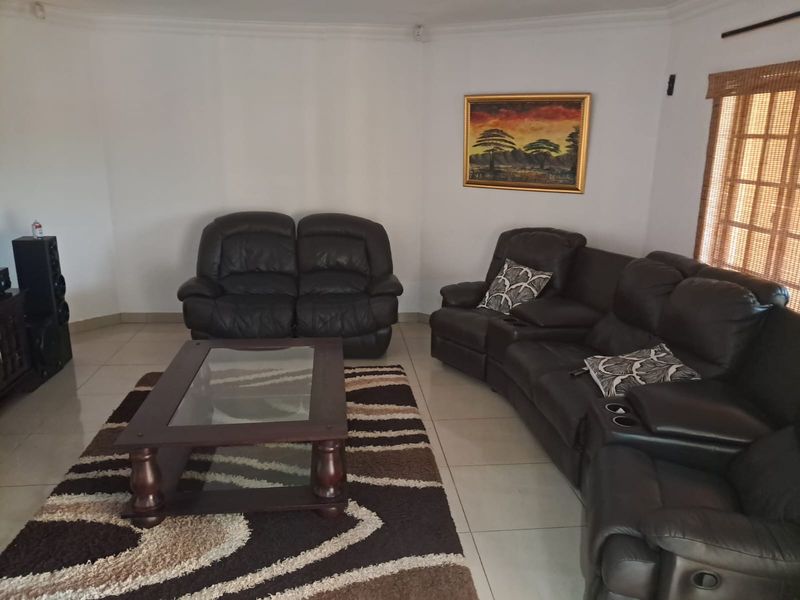 A spacious living room featuring neutral tiled flooring, coved cornicing, and a large window with a bamboo blind, offering a comfortable and functional living space.