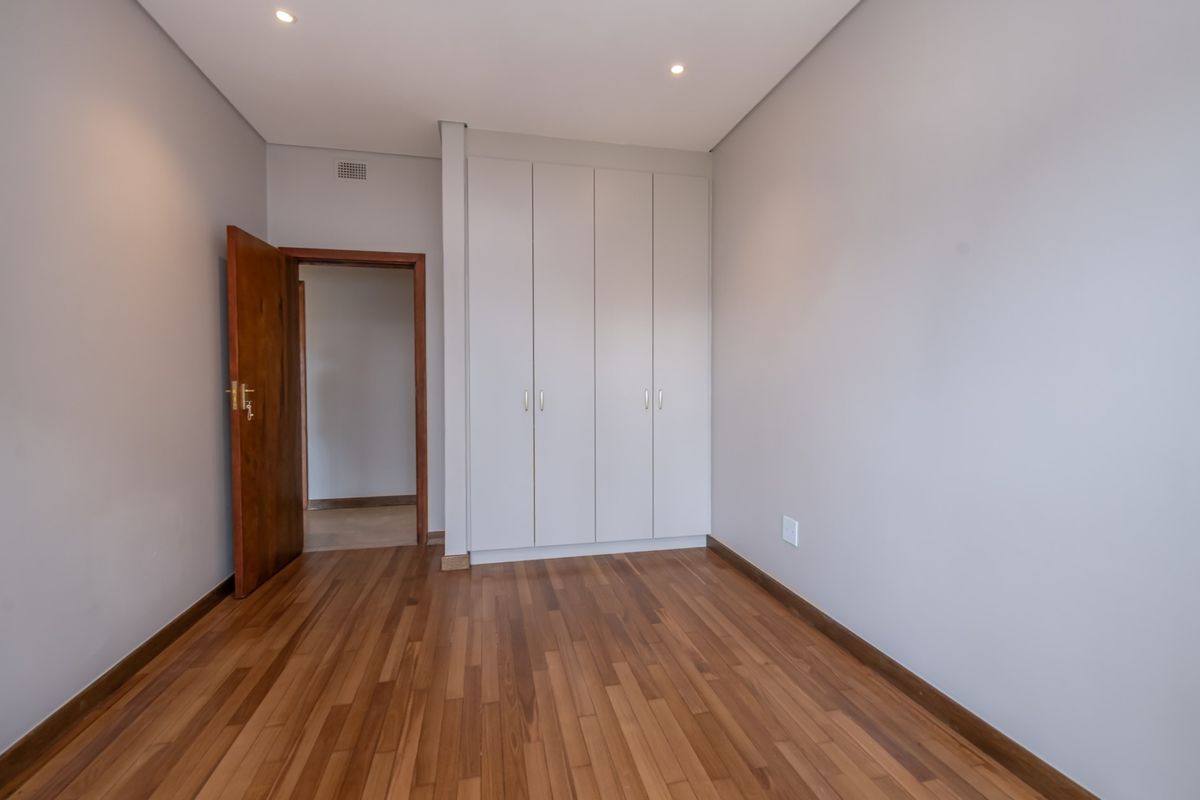 A clean, empty bedroom featuring polished timber flooring, neutral walls, recessed downlighting, and ample built-in cupboard storage.