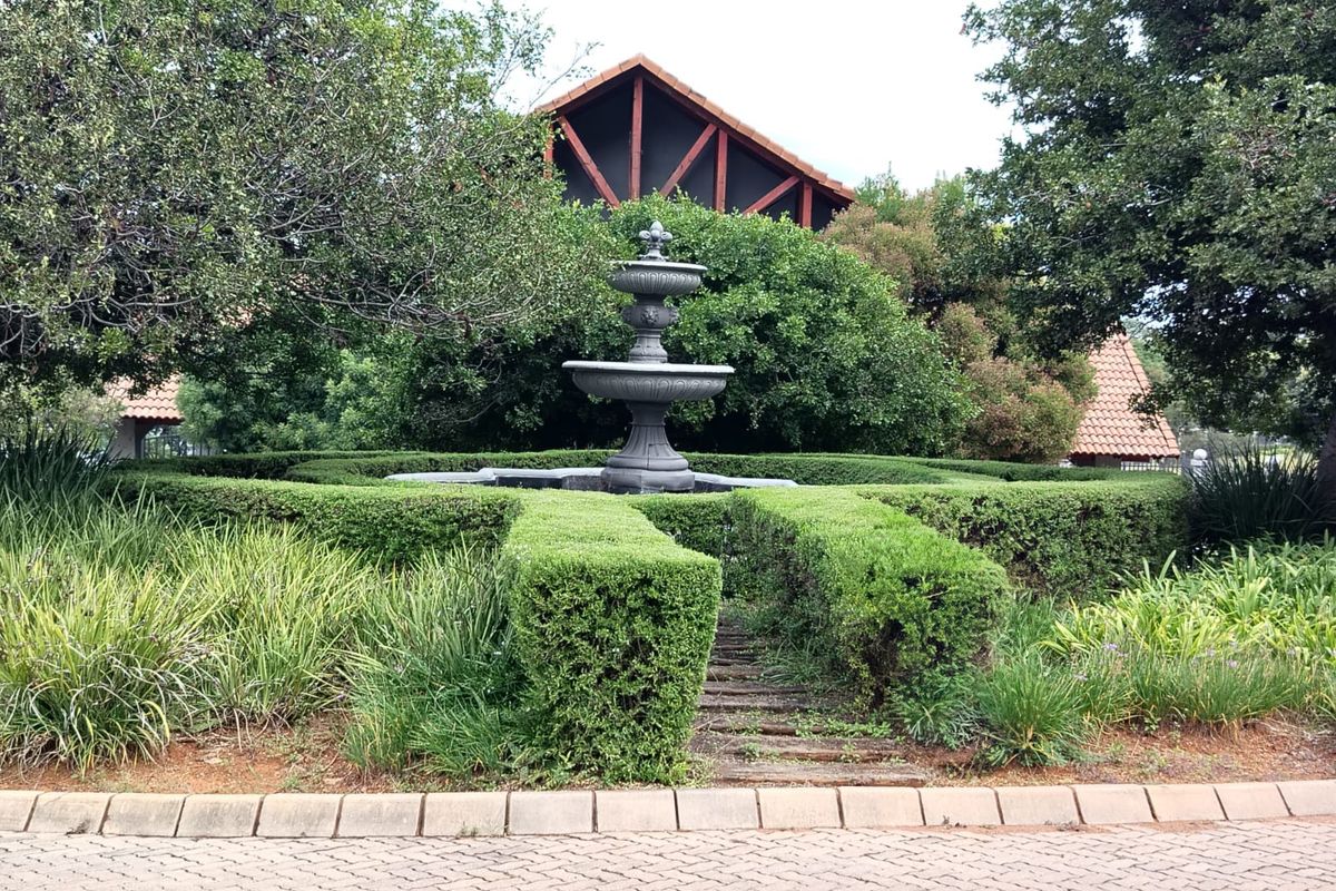 A well-maintained garden area featuring a central stone fountain surrounded by manicured hedges and mature landscaping.