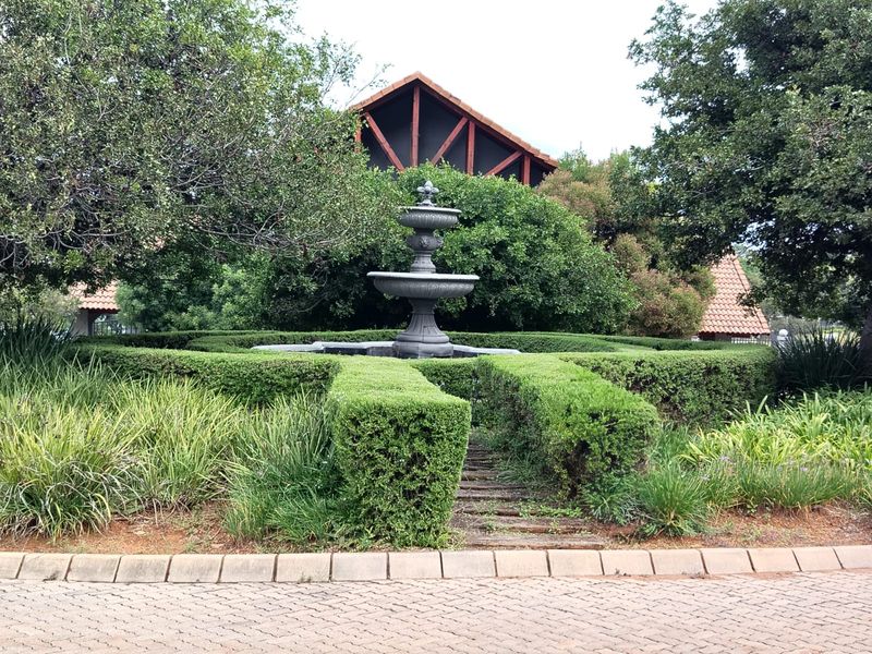 A well-maintained garden area featuring a central stone fountain surrounded by manicured hedges and mature landscaping.