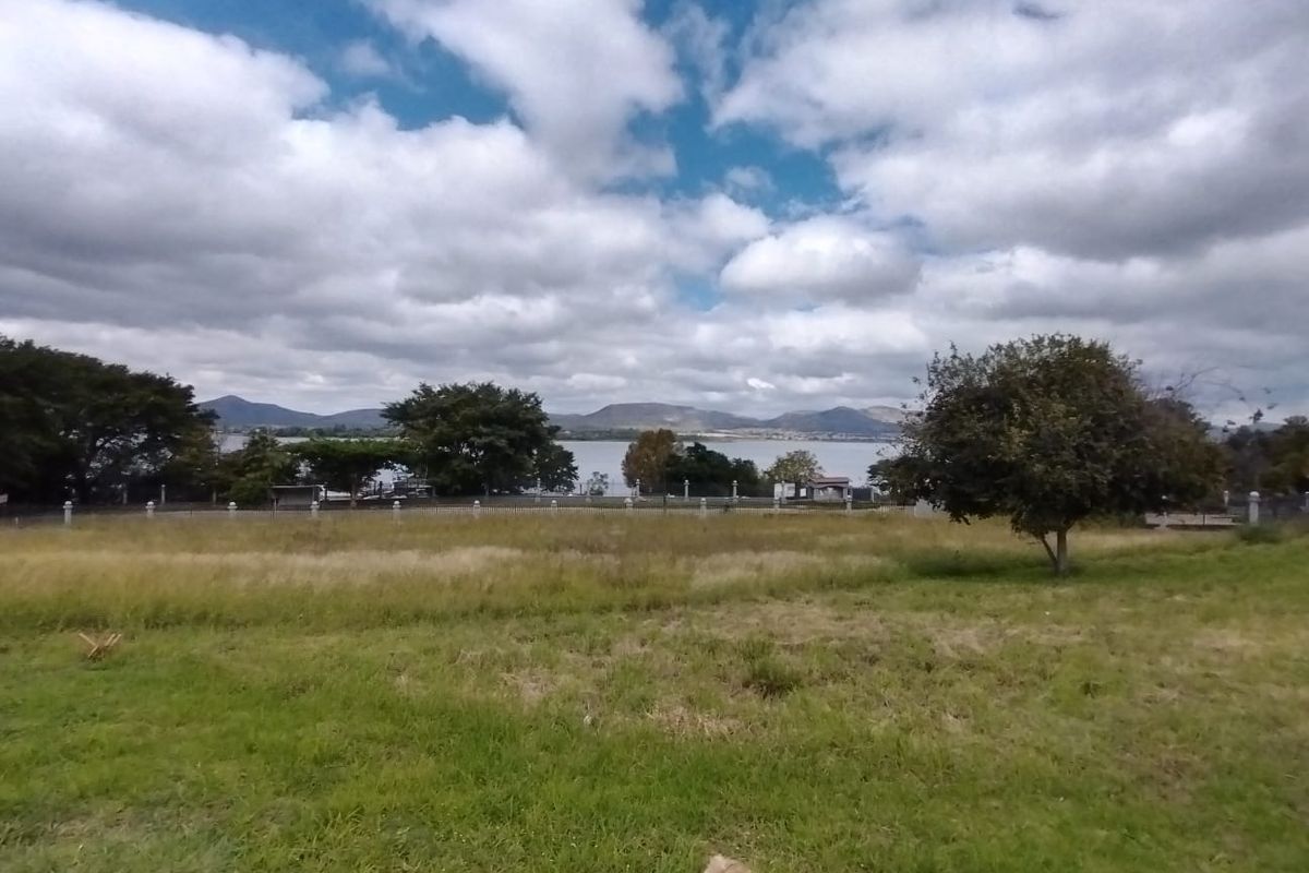 A scenic view of a lake and distant mountains from a vacant residential plot with established perimeter fencing.