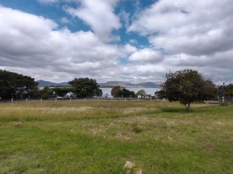 A scenic view of a lake and distant mountains from a vacant residential plot with established perimeter fencing.