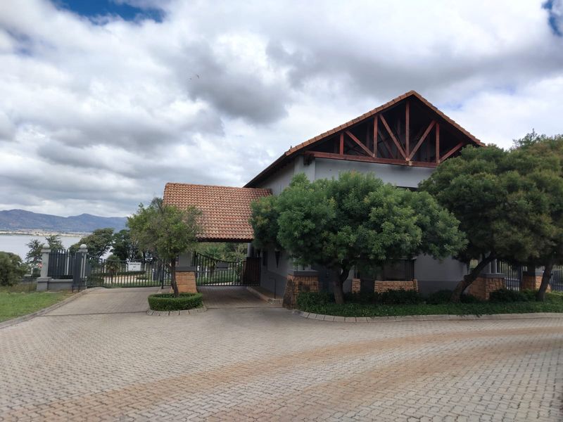 Front view of the residential estate entrance featuring a paved driveway, security gate, and a building with stone cladding and tiled roof.