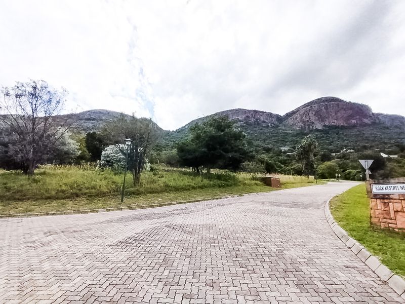 A view of a paved residential street entrance featuring stone signage and scenic mountain views in the background.