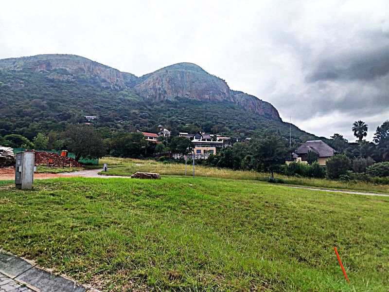 A scenic view of a vacant residential plot featuring expansive green grass with a prominent mountain backdrop.
