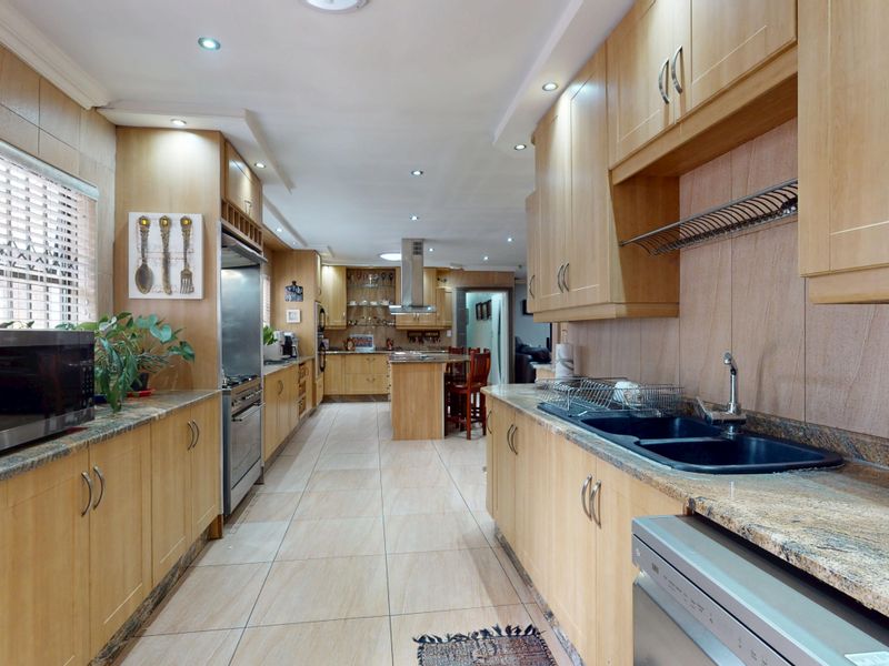 Spacious kitchen featuring light wood cabinetry, granite countertops, tiled flooring, and integrated stainless steel appliances with ample storage and workspace.