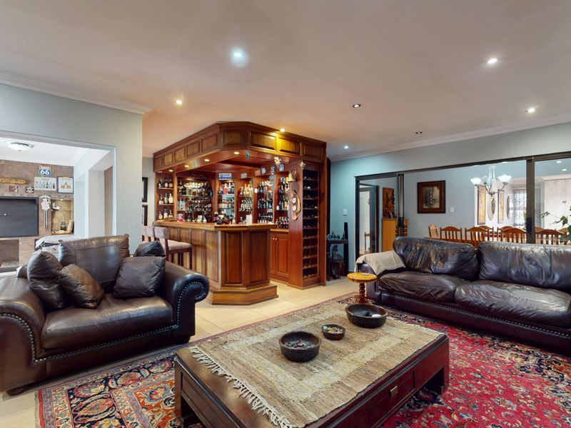 Spacious open-plan living area featuring a custom built-in wooden bar with integrated wine storage, recessed lighting, and a cozy fireplace in the adjacent space.