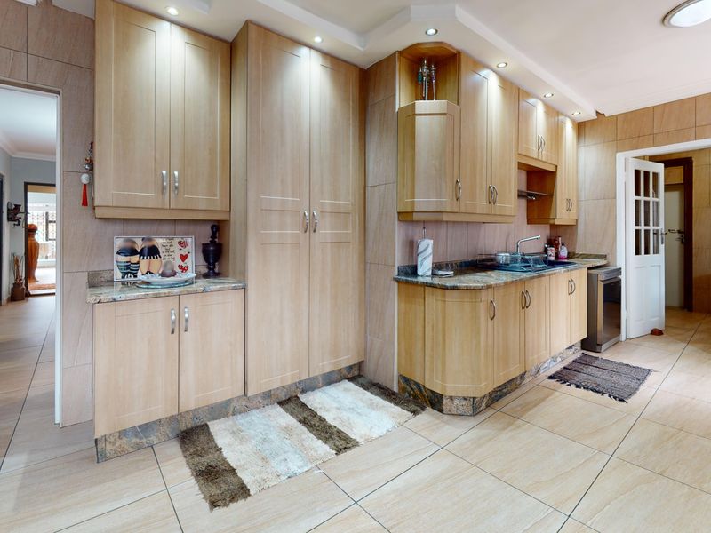 A functional kitchen featuring light wood-toned cabinetry, granite countertops, integrated sink, and neutral floor-to-ceiling wall tiling with recessed lighting.