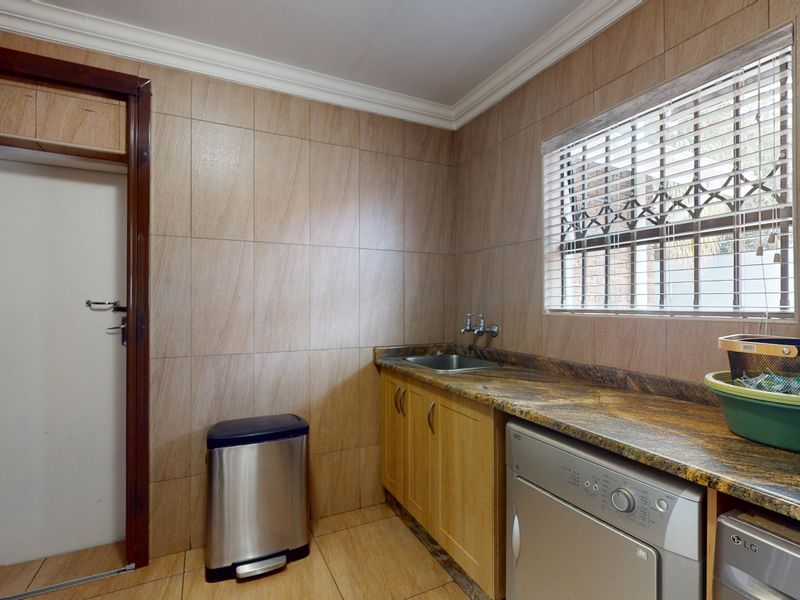 A functional laundry room featuring tiled walls, granite countertops, built-in cabinetry, and a stainless steel sink with space for laundry appliances.