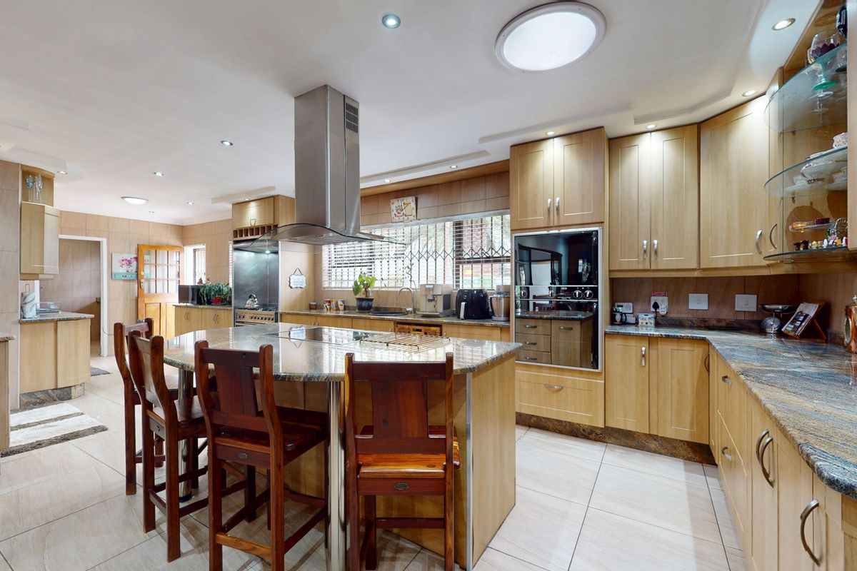 Spacious kitchen featuring light wood cabinetry, granite countertops, a central island with seating, built-in appliances, and a skylight for natural illumination.