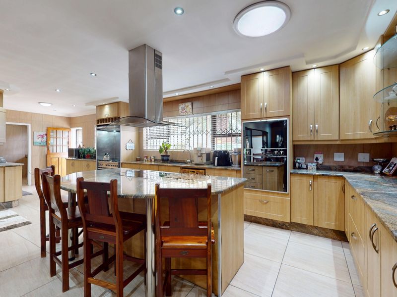 Spacious kitchen featuring light wood cabinetry, granite countertops, a central island with seating, built-in appliances, and a skylight for natural illumination.