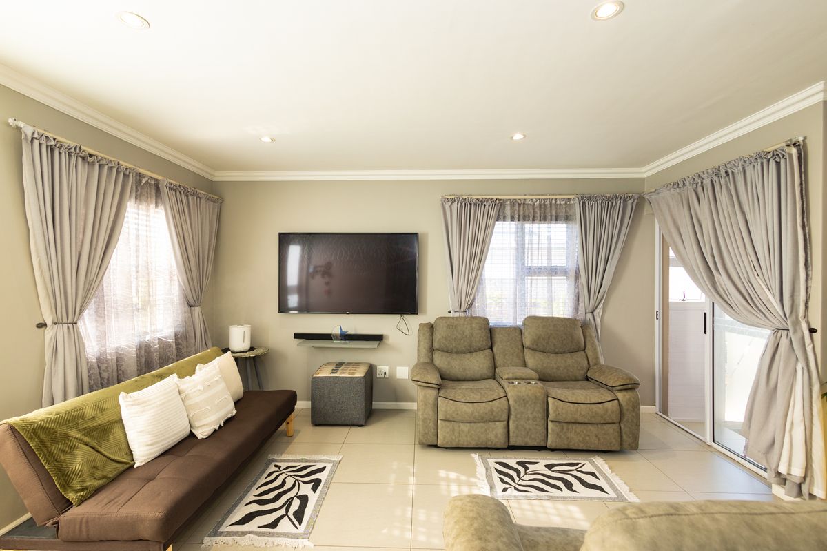 A well-maintained living room featuring neutral wall tones, tiled flooring, recessed lighting, crown molding, and a sliding glass door providing natural light.