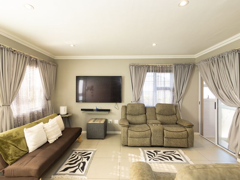 A well-maintained living room featuring neutral wall tones, tiled flooring, recessed lighting, crown molding, and a sliding glass door providing natural light.