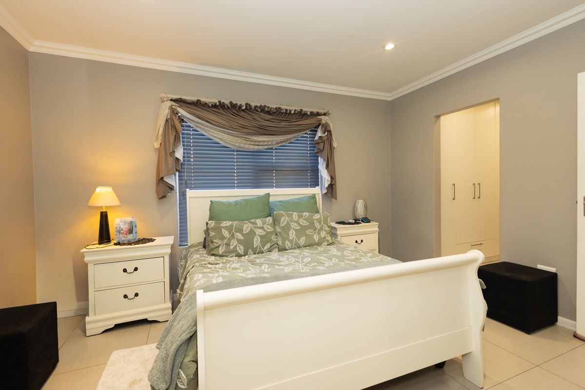 A well-maintained bedroom featuring neutral grey walls, tiled flooring, recessed downlighting, and built-in cupboards with a clean, modern finish.