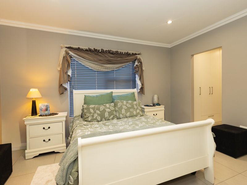 A well-maintained bedroom featuring neutral grey walls, tiled flooring, recessed downlighting, and built-in cupboards with a clean, modern finish.