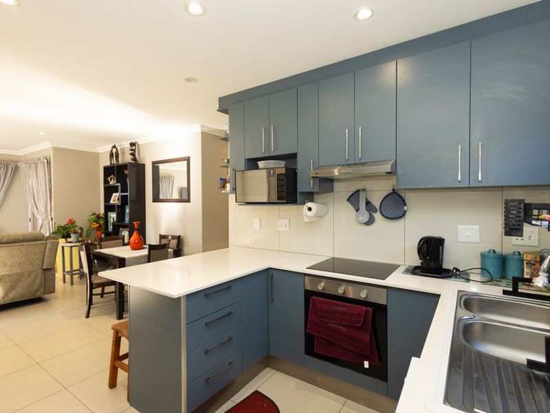 Modern open-plan kitchen featuring blue cabinetry, quartz countertops, integrated appliances, and tiled flooring, seamlessly flowing into the adjacent dining and living area.