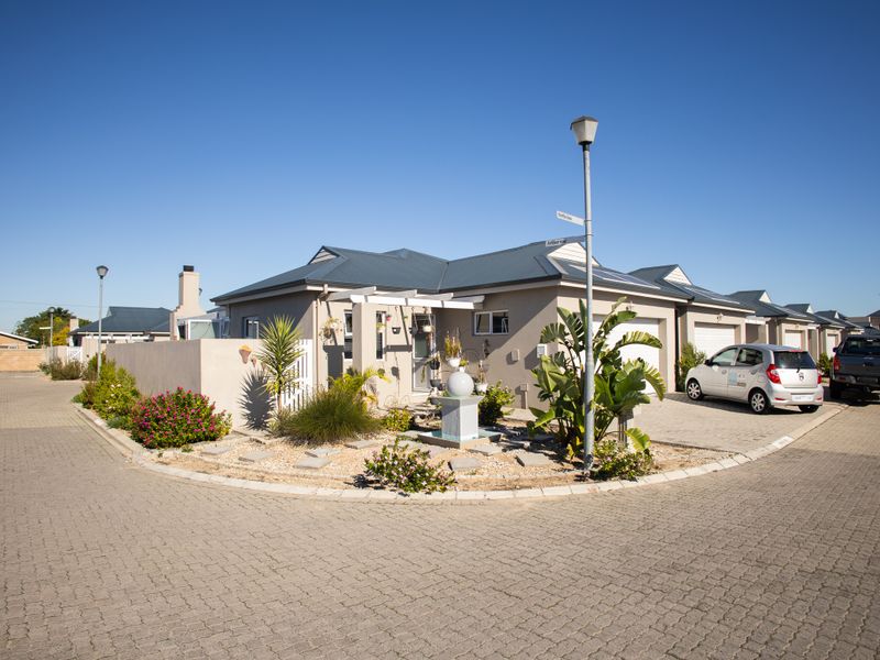 A well-maintained residential property featuring a paved driveway, attached garage, and a landscaped front garden area with a pergola.