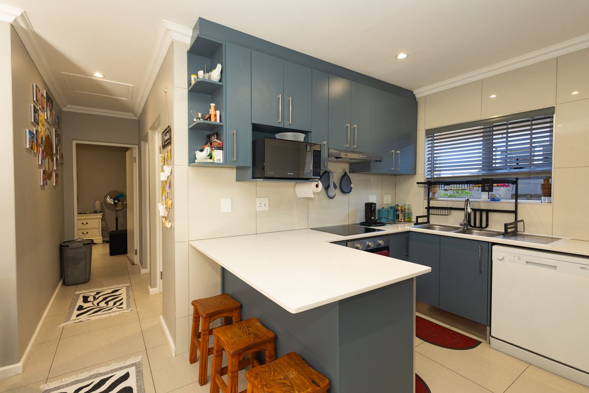 Modern kitchen featuring blue cabinetry, stone countertops, integrated appliances, and a breakfast bar, seamlessly connected to the hallway.