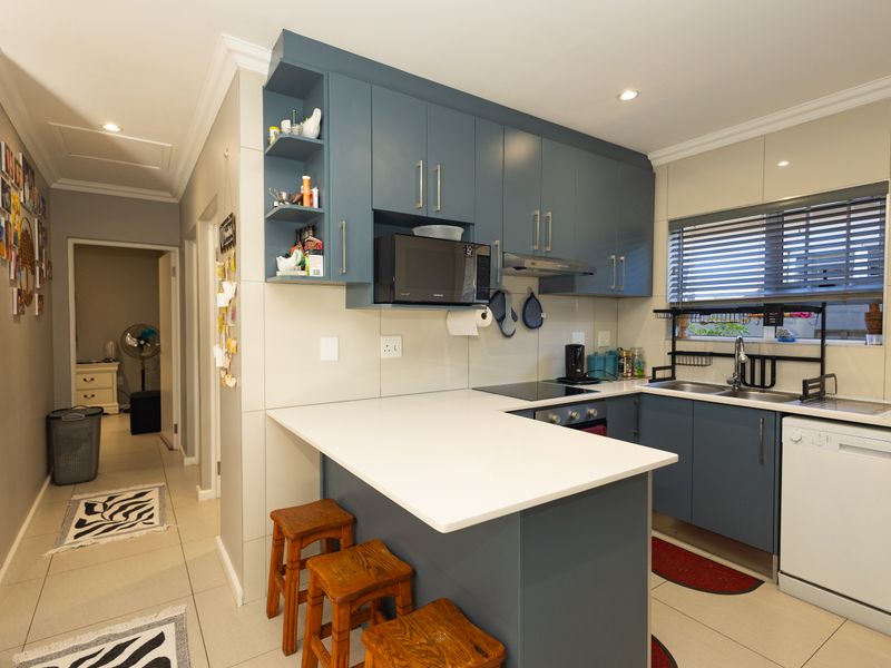 Modern kitchen featuring blue cabinetry, stone countertops, integrated appliances, and a breakfast bar, seamlessly connected to the hallway.