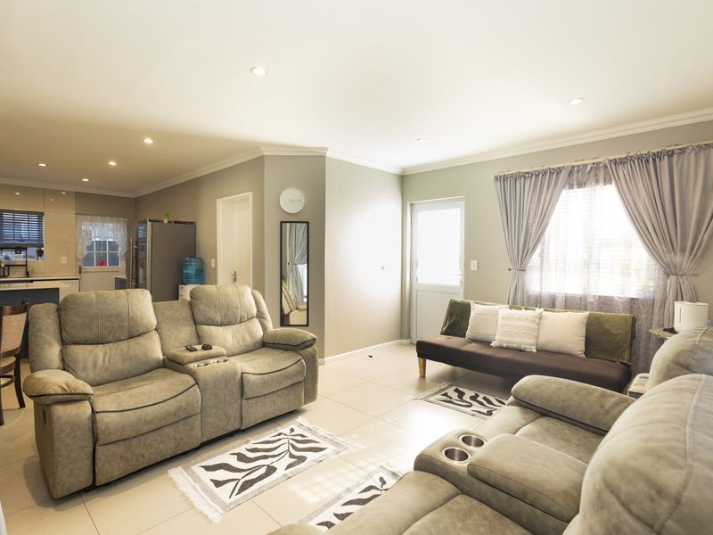 Spacious open-plan living area featuring tiled floors, recessed lighting, and a modern kitchen with island, seamlessly connecting to the outdoor entrance.