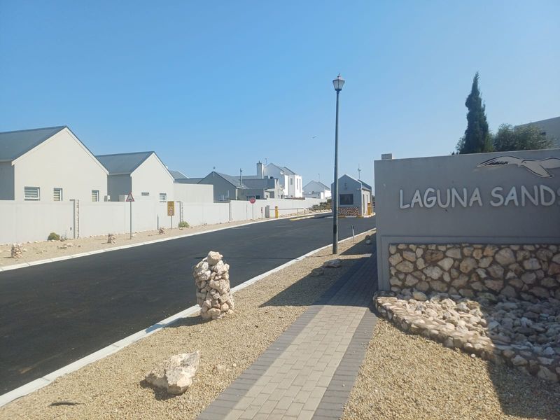 Entrance view of Laguna Sands residential estate featuring a paved road, security gatehouse, and perimeter boundary wall.
