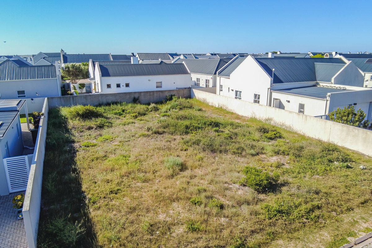 An aerial view of a vacant residential plot enclosed by perimeter boundary walls, situated within a developed residential estate.