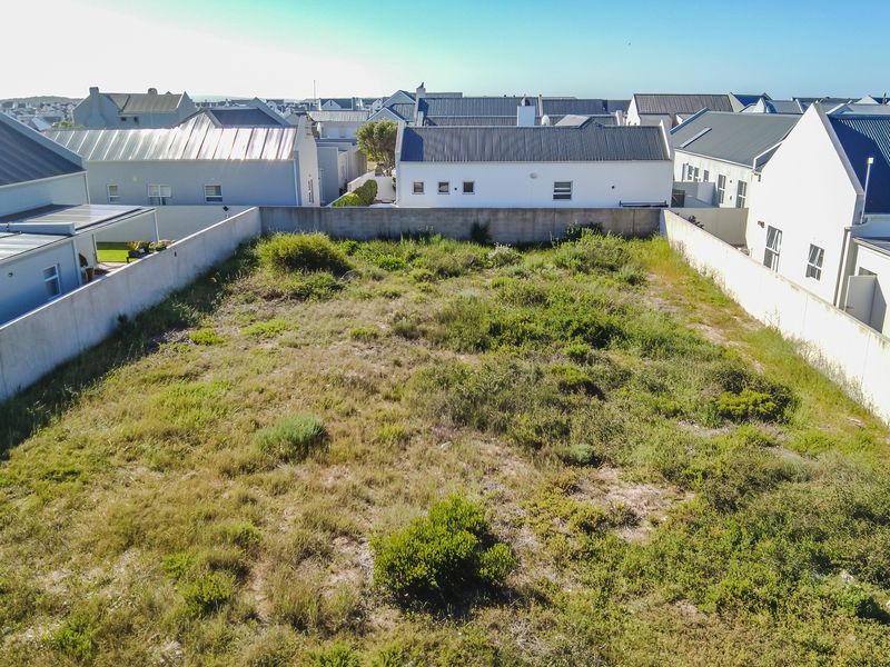 An aerial view of a vacant residential plot enclosed by boundary walls, situated within a developed residential estate.