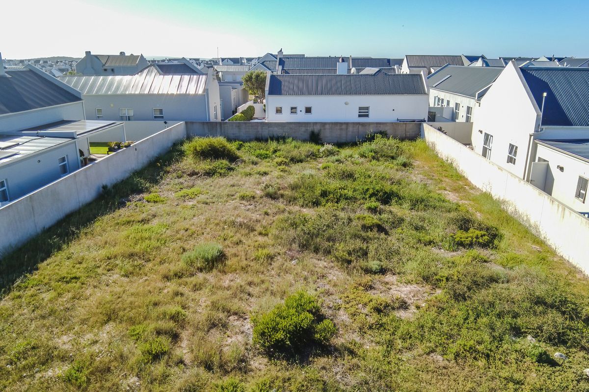 An aerial view of a vacant residential plot enclosed by boundary walls, situated within a developed residential estate.