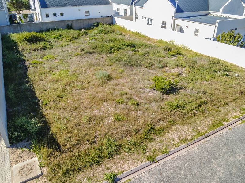 An aerial view of a vacant residential plot featuring boundary walls and direct street access, ready for development.