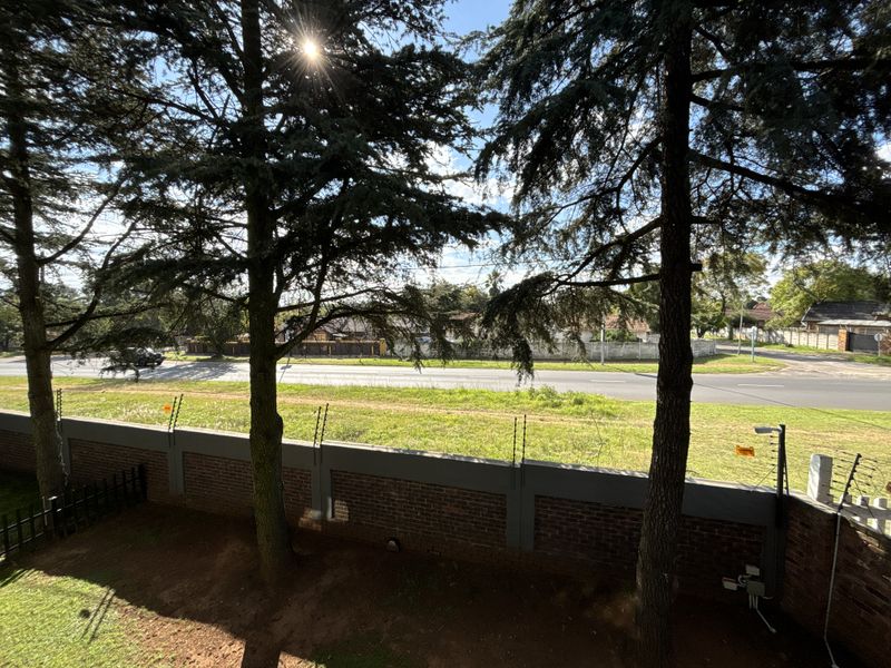 An elevated view overlooking a street, featuring a brick boundary wall with integrated electric fencing and mature trees.