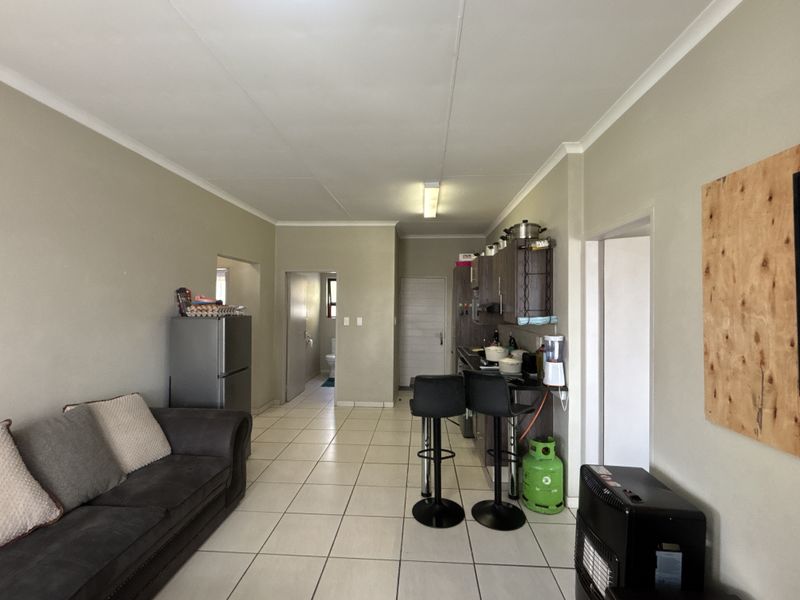 Open-plan living and kitchen area featuring tiled flooring, built-in cabinetry, and a breakfast counter, requiring minor cosmetic updates to improve the overall aesthetic.