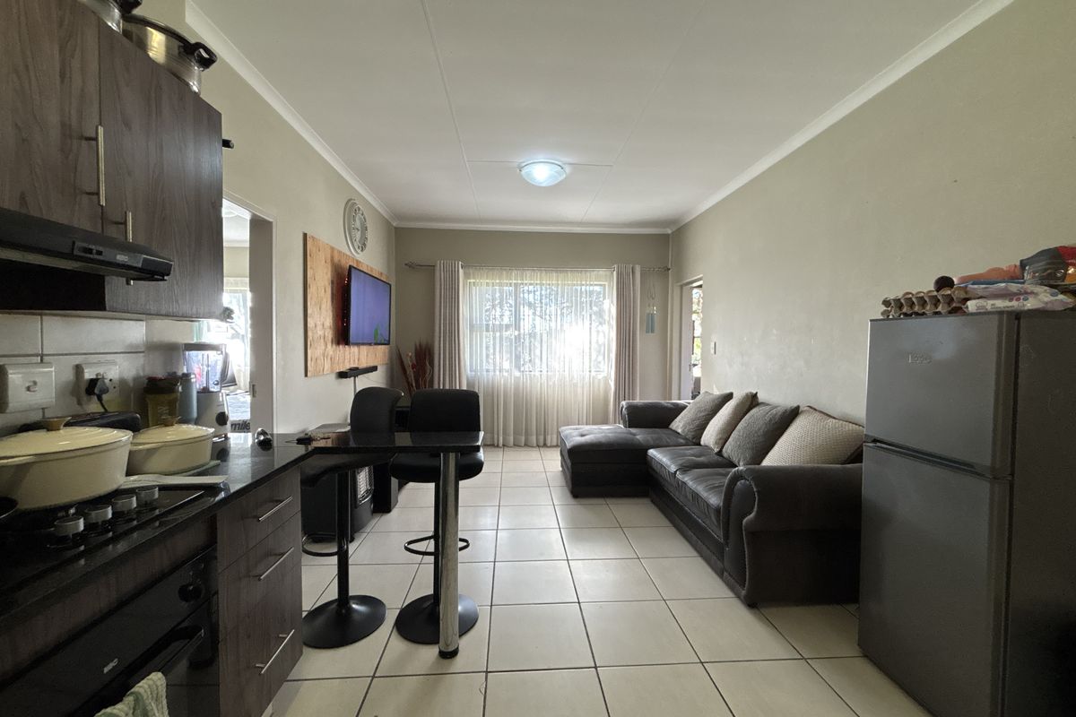 Open-plan living area featuring a compact kitchen with built-in oven and hob, flowing into a comfortable lounge space with tiled flooring throughout.