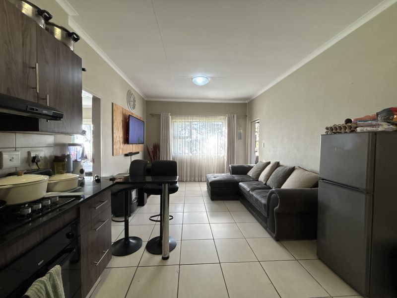 Open-plan living area featuring a compact kitchen with built-in oven and hob, flowing into a comfortable lounge space with tiled flooring throughout.
