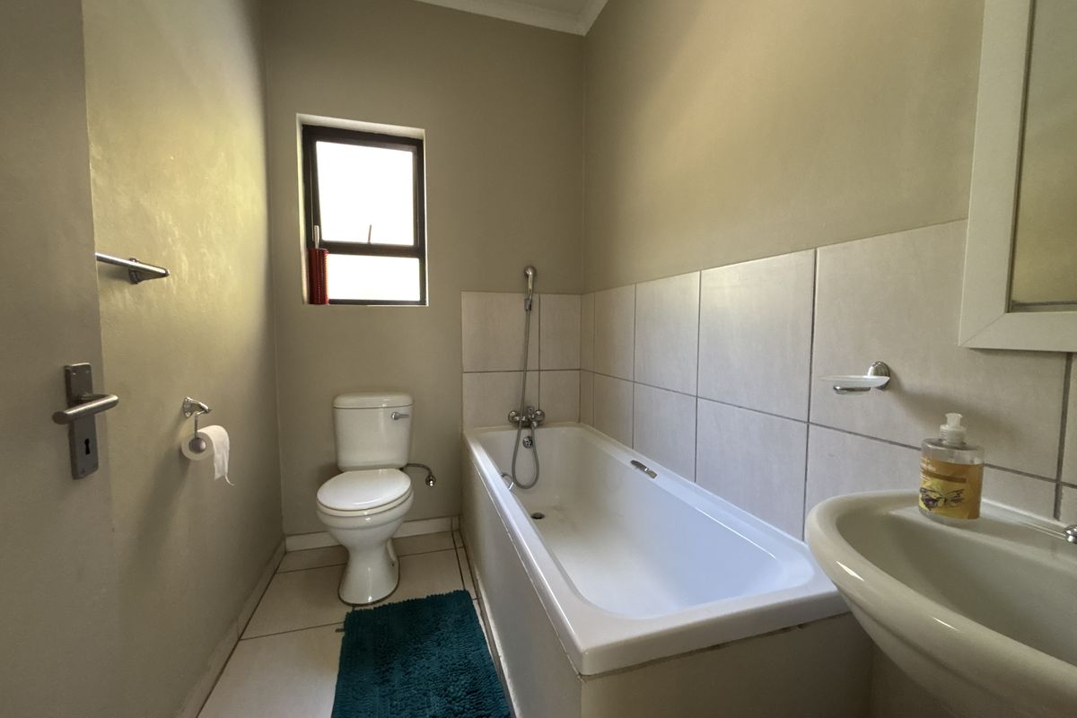 A functional bathroom featuring a bathtub, pedestal basin, and toilet with neutral wall and floor tiling.