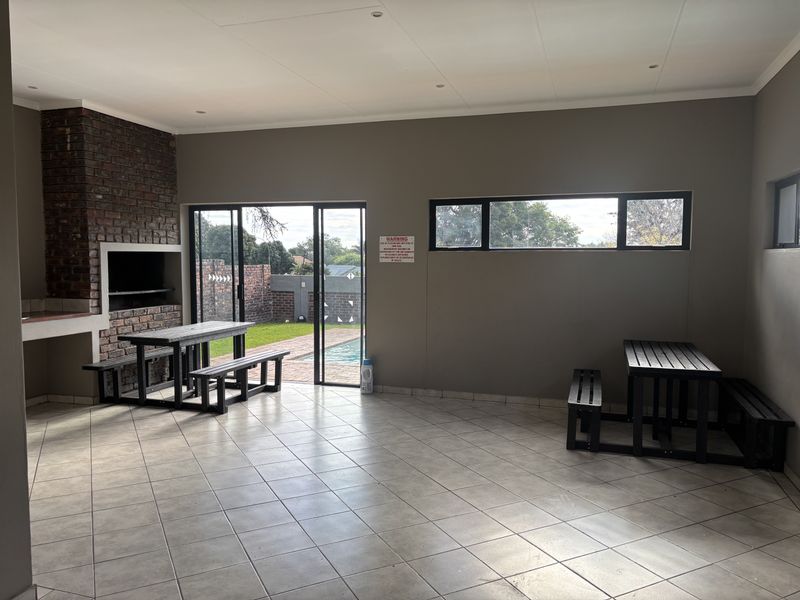 Spacious covered patio featuring a built-in brick braai, tiled flooring, and sliding glass doors providing direct access to the pool area.