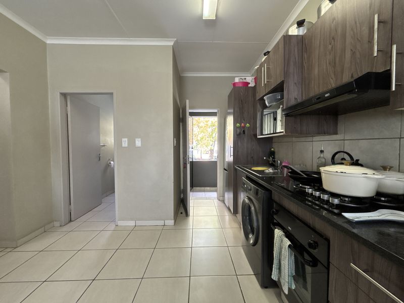 Functional kitchen featuring dark wood cabinetry, granite countertops, integrated oven, gas hob, and tiled flooring with direct access to an exterior area.