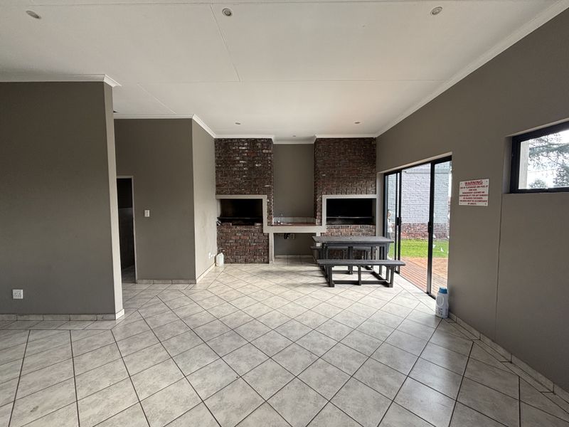 Covered patio area featuring a built-in brick braai, prep sink, and tiled flooring, with sliding glass doors providing access to the garden.