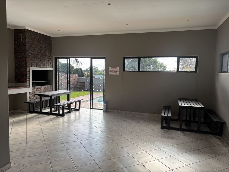 Spacious covered patio featuring a built-in brick braai, tiled flooring, and sliding doors opening to the pool area.