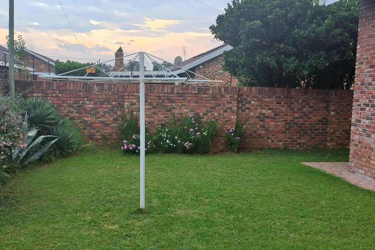 A private rear garden featuring a well-maintained lawn, a brick boundary wall, and a paved walkway adjacent to the townhouse structure.
