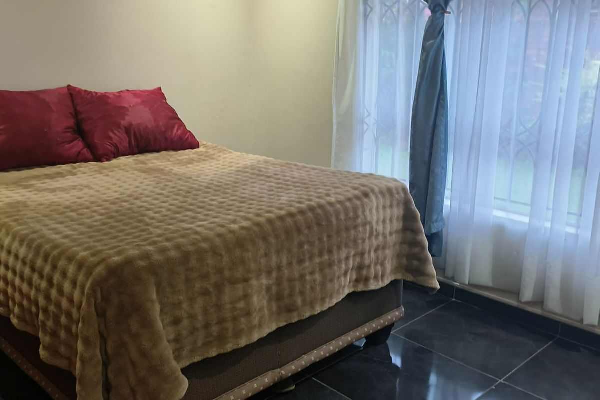 A bedroom featuring dark tiled flooring and a large window fitted with a security gate, providing natural light.