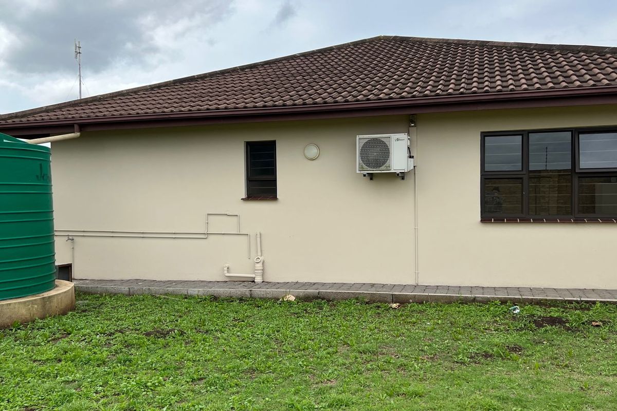 Rear exterior view of the house featuring a water tank, wall-mounted air conditioning unit, paved walkway, and tiled roof.