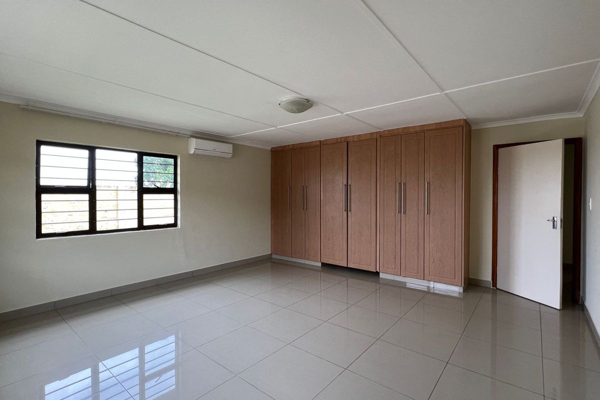 Spacious bedroom featuring neutral tiled flooring, extensive built-in wooden cupboards, and a wall-mounted air conditioning unit.
