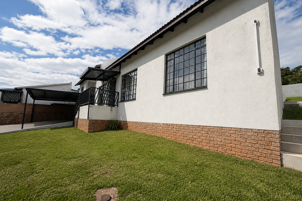 A view of the side and rear exterior of the house, featuring a lawn, brick base, and metal-framed windows.