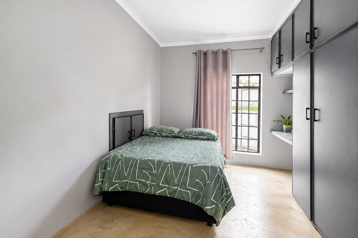 A well-lit bedroom featuring built-in dark cabinetry, polished concrete flooring, and a window with security bars.