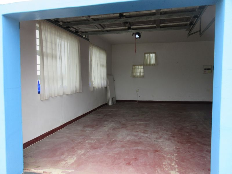 A spacious, empty garage featuring a concrete floor, sectional door mechanism, and an electrical distribution board.
