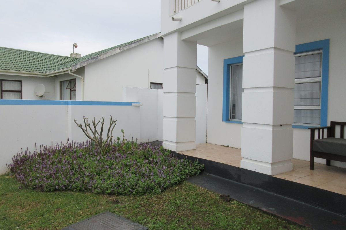 A rear exterior view of the house featuring a tiled patio, a small landscaped garden, and a balcony with metal railings.