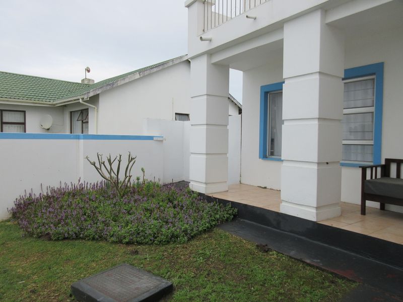 A rear exterior view of the house featuring a tiled patio, a small landscaped garden, and a balcony with metal railings.