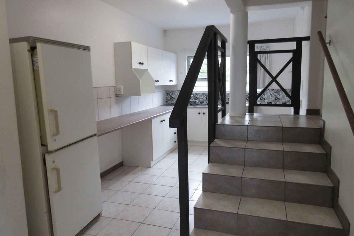 A functional kitchen area featuring white cabinetry, tiled flooring, and a staircase leading to the upper level.