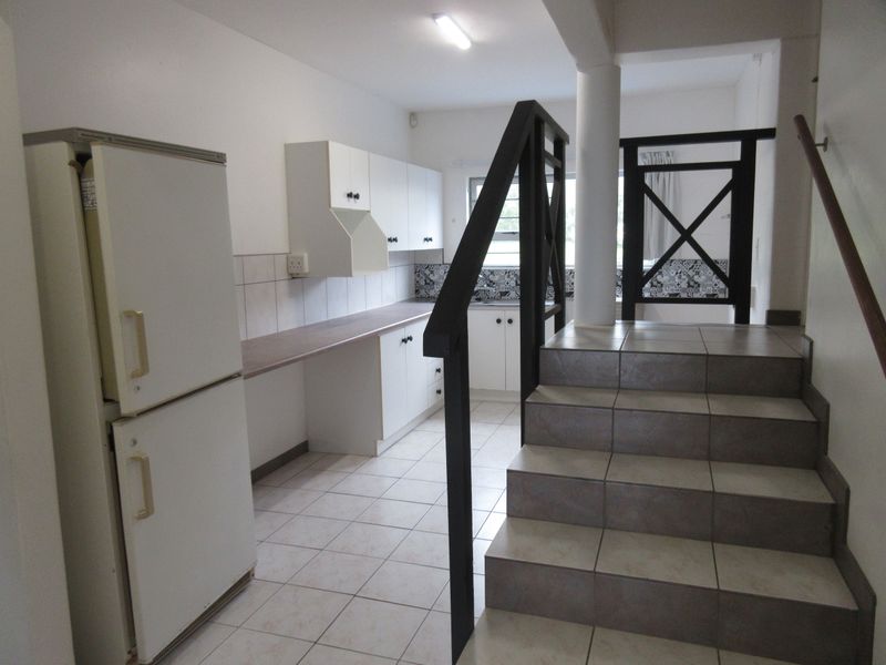 A functional kitchen area featuring white cabinetry, tiled flooring, and a staircase leading to the upper level.