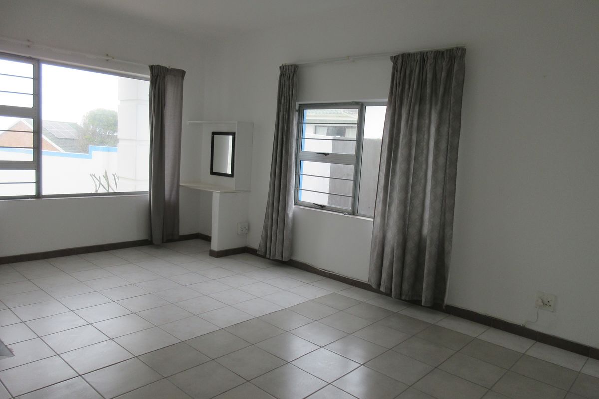 A spacious, empty bedroom featuring neutral tiled flooring, large windows with security bars, and a built-in vanity shelf.